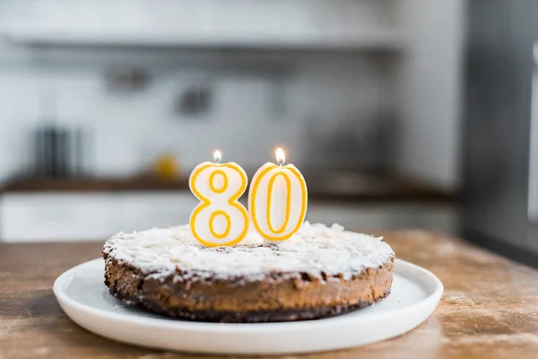 Selective focus of delicious birthday cake with burning candles and '80' sign on top — Stock Photo