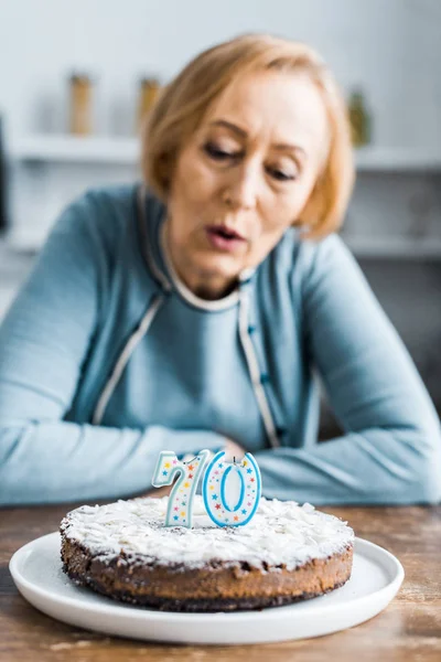 Foco seletivo de bolo com sinal '70' no topo e mulher sênior em segundo plano durante a celebração de aniversário — Fotografia de Stock