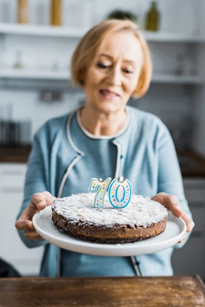 Selective focus of cake with '70' sign on top and senior woman on background during birthday celebration — Stock Photo
