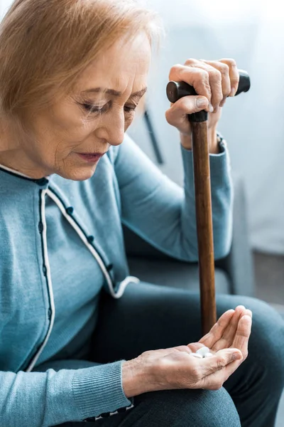 Sick senior woman with walking stick holding medicine in hand — Stock Photo