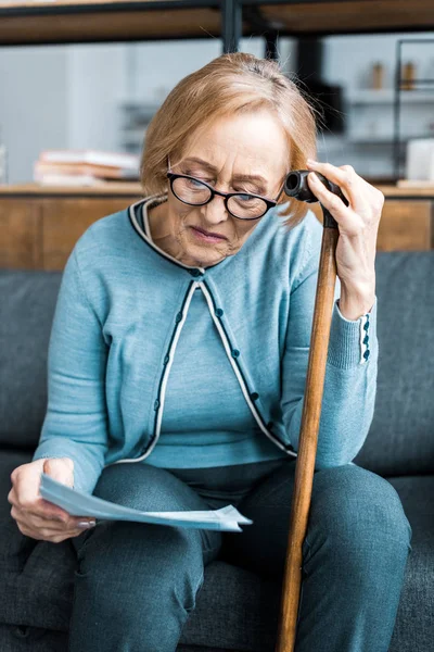 Senior woman with walking stick looking at tax form at home — Stock Photo