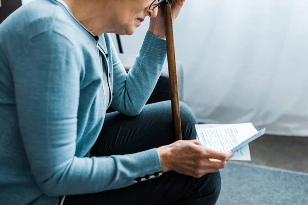 Cropped view of senior woman with walking stick looking at tax form at home — Stock Photo