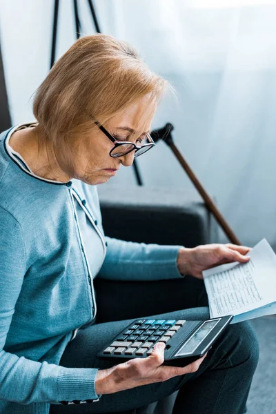 Focalizzazione selettiva della donna anziana seduta sul divano con calcolatrice e conteggio delle fatture a casa — Foto stock