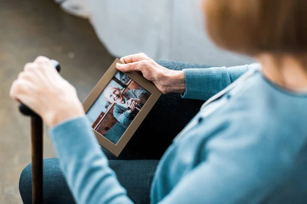 Cropped view of senior woman sitting with walking stick and looking at frame with man on photograph — Stock Photo