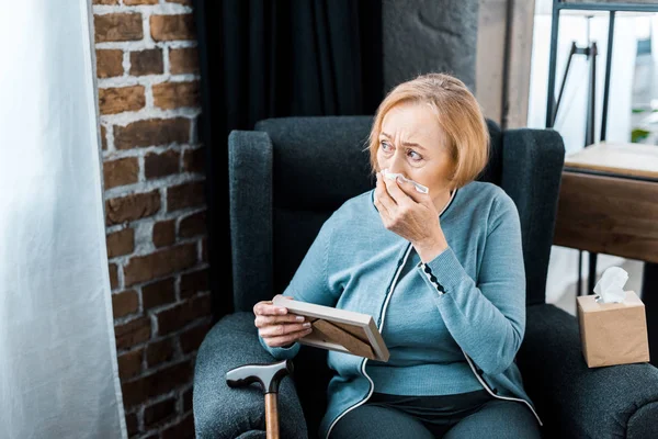 Bouleversé femme âgée essuyant le visage des larmes, pleurant et tenant cadre photo à la maison — Photo de stock