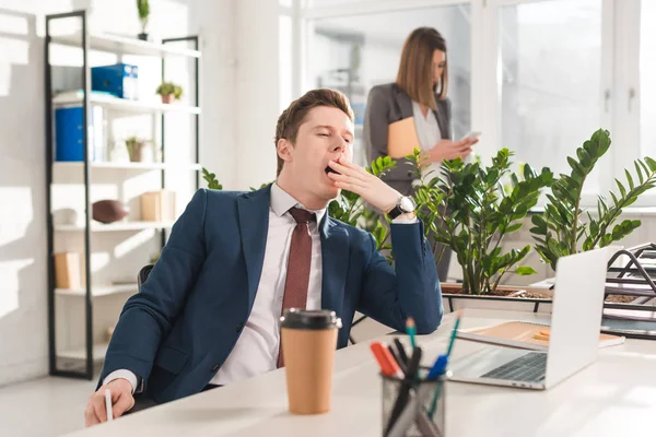 Selective focus of tired businessman yawning near female coworker on background — Stock Photo