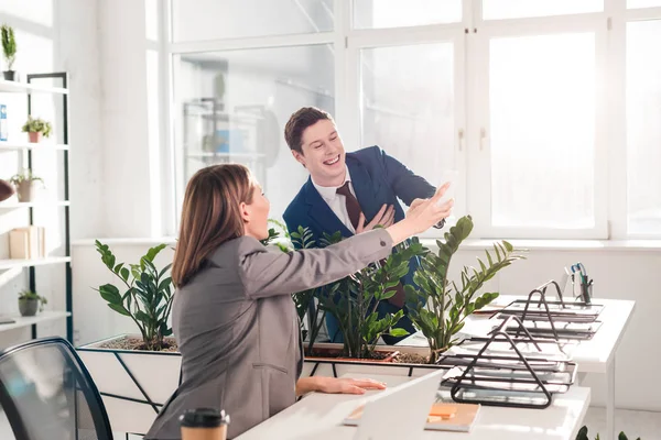 Empresaria sosteniendo teléfono inteligente y riendo con su compañero de trabajo en la oficina - foto de stock