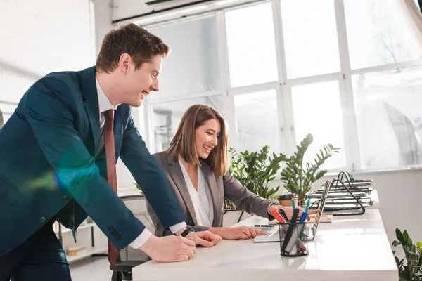 Щаслива бізнес-леді сміється з колегою біля ноутбука в офісі — стокове фото