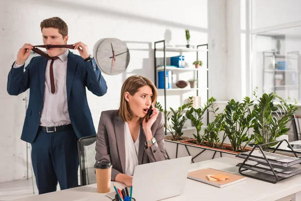 Attractive businesswoman talking on smartphone near coworker in office,  procrastination concept — Stock Photo