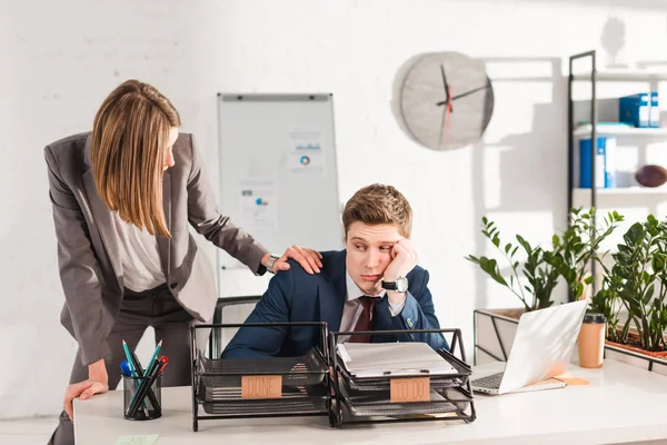 Donna d'affari in piedi vicino all'uomo assonnato seduto alla scrivania vicino a vassoi di documenti con lettering, concetto di procrastinazione — Foto stock