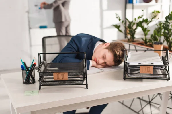 Selektive Fokussierung der Dokumentenablagen mit Schriftzug in der Nähe des am Schreibtisch schlafenden Geschäftsmannes, Verzögerungskonzept — Stockfoto