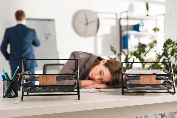 Selective focus of document trays with lettering near woman sleeping at desk near, procrastination concept — Stock Photo