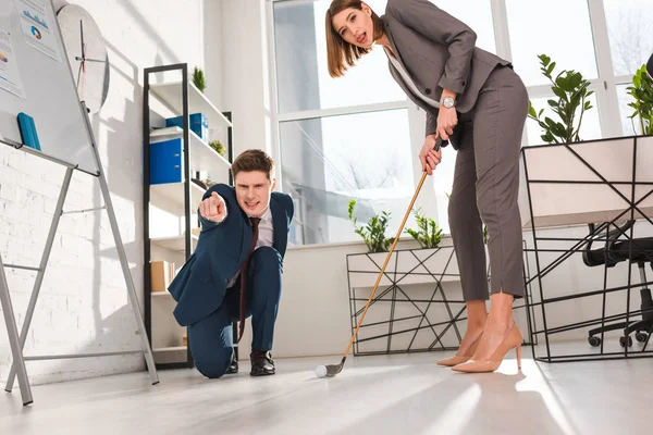 Empresário emocional apontando com o dedo enquanto colega de trabalho do sexo feminino jogar mini golfe no escritório — Fotografia de Stock