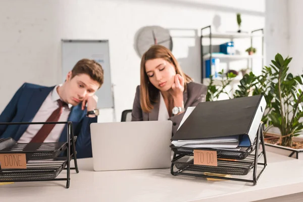 Selective focus of document trays with lettering near sleepy coworkers, procrastination concept — Stock Photo