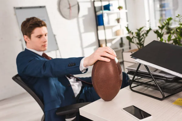 Selective focus of rugby ball in hand of businessman in office — Stock Photo