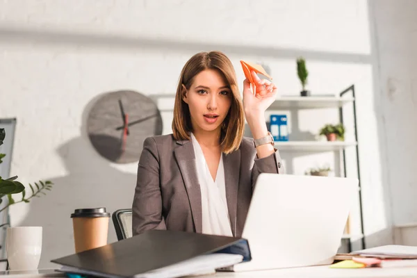 Selective focus of attractive businesswoman holding paper plane in office, procrastination concept — Stock Photo