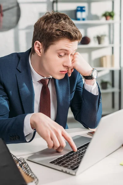 Guapo hombre de negocios agotado sentado cerca de la computadora portátil en la oficina - foto de stock