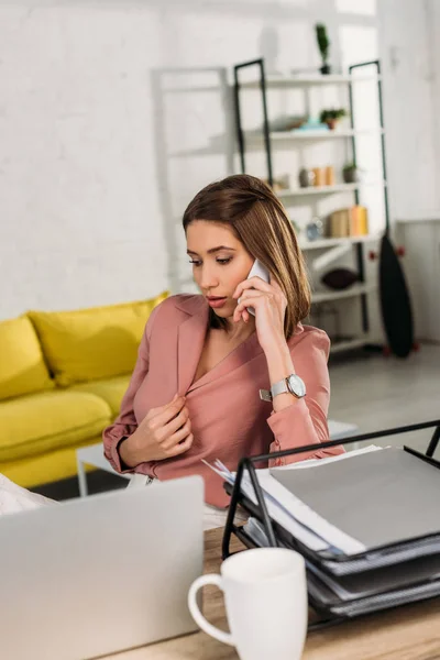 Nachdenkliche Frau, die zu Hause am Laptop sitzt und auf dem Smartphone spricht — Stockfoto