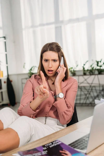 Selective focus of shocked woman talking on smartphone while looking at nail at home — Stock Photo