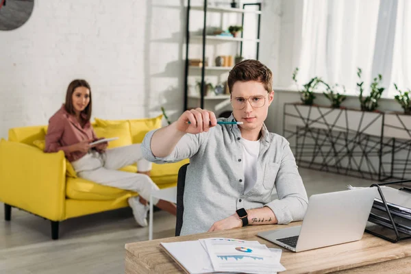 Man looking at pencil near laptop with girlfriend on background — Stock Photo