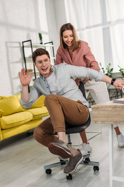 Cheerful woman smiling while pushing chair of scared boyfriend — Stock Photo