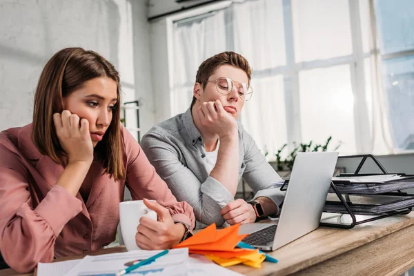 Traurige Frau hält Tasse mit Getränk in der Nähe ihres Freundes und schaut auf Laptop — Stockfoto