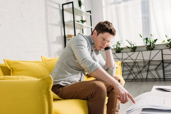 Müder Mann mit Brille sitzt auf Sofa und zeigt mit dem Finger auf Dokument — Stockfoto