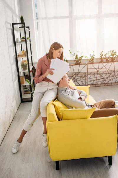 Attraktive Frau hält Dokumente in Händen und gähnt neben Freund, der zu Hause auf Sofa schläft — Stockfoto