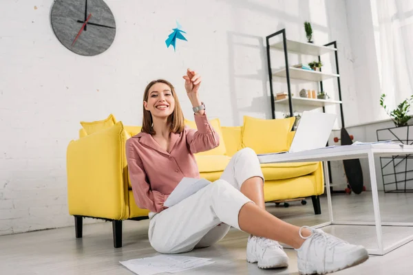Cheerful woman sitting on floor and playing with paper plane at home — Stock Photo