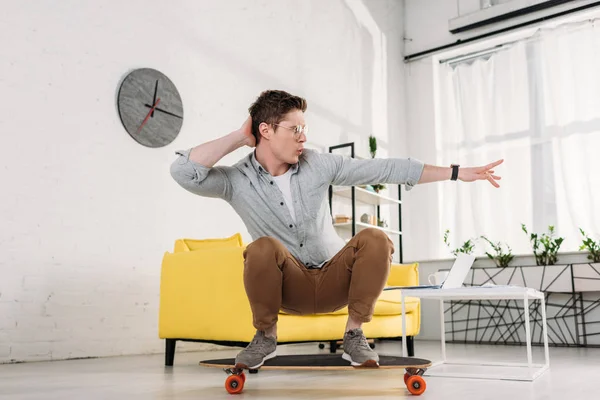 Funny man in glasses riding skateboard at home — Stock Photo