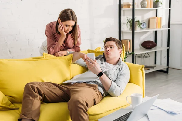 Müde Frau schaut Freund mit Smartphone an, während sie auf Sofa liegt — Stockfoto