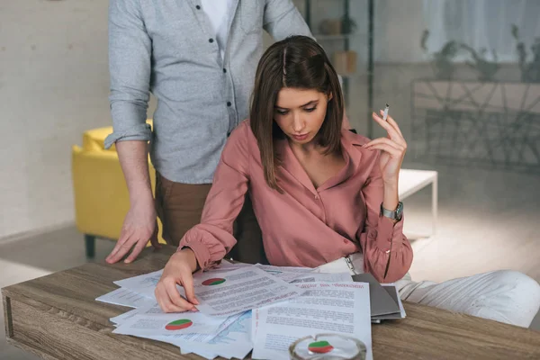 Woman holding cigarette and looking at charts and graphs near man — Stock Photo