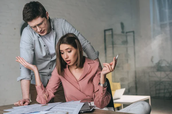 Woman holding cigarette while looking at charts and graphs near concentrated man — Stock Photo