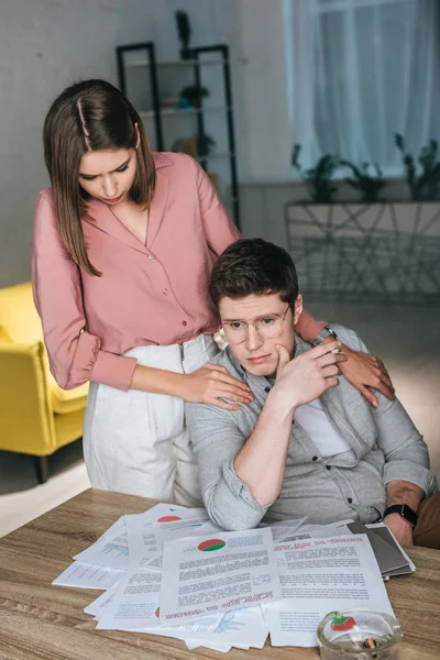 Woman standing near pensive man in glasses holding cigarette near charts and graphs — Stock Photo