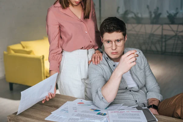 Vista recortada de la mujer sosteniendo papel cerca de hombre reflexivo sosteniendo cigarrillo - foto de stock