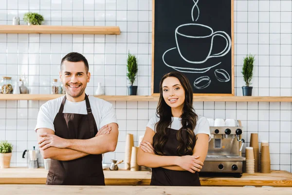 Cashiers standing behind wooden bar counter and smiling in coffee house — Stock Photo
