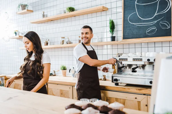 Barista fazendo café e sorrindo wile caixa atraente trabalhando atrás do balcão de bar na casa de café — Fotografia de Stock