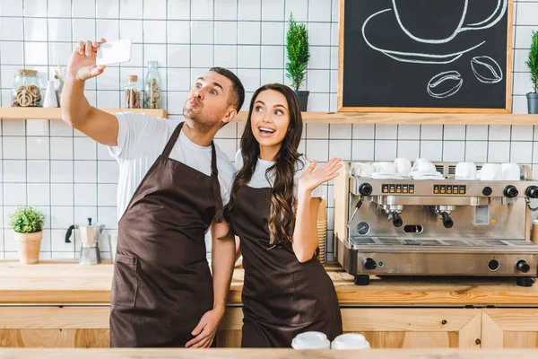 Cassieri in grembiuli marroni in piedi e scattare selfie in caffetteria — Foto stock