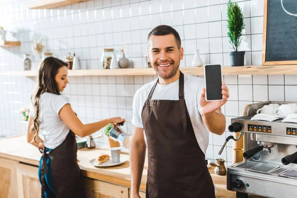 Красивый кассир показывает смартфон с чистым экраном, коварная брюнетка бариста работает в кофейне — стоковое фото