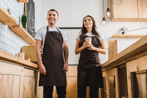 Cashiers standing and smiling behind wooden bar counter in coffee house — Stock Photo