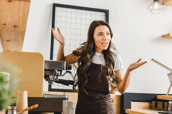 Angry brunette barista in brown apron standing near coffee machine in coffee house — Stock Photo