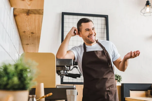 Sorrir bonito barista em avental marrom em pé perto da máquina de café na casa de café — Fotografia de Stock