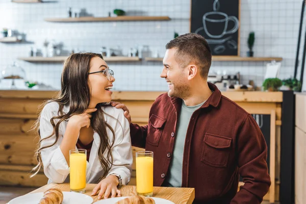 Приваблива брюнетка жінка і красивий чоловік у бордовій сорочці, сидячи за столом, сміючись і дивлячись один одному в кав'ярні — стокове фото