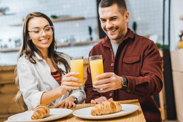 Selective focus of glasses with juice in woman and man hands sitting at table with croissants in coffee house — Stock Photo