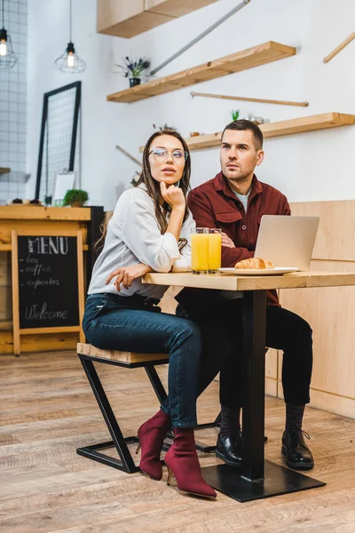 Hermosa mujer morena y hombre guapo sentado a la mesa con jugo en vasos y portátil en la cafetería - foto de stock