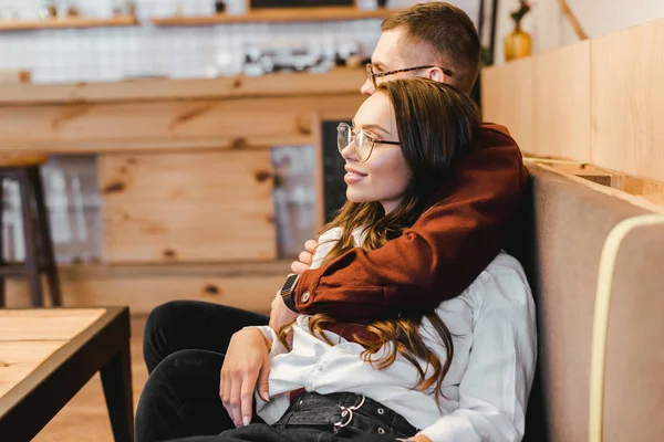 Attractive woman and man sitting on couch at table and hugging in coffee house — Stock Photo