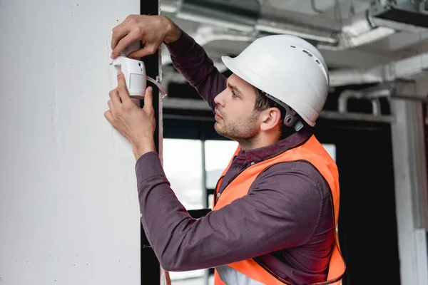 Serious firefighter in uniform and helmet checking fire alarm — Stock Photo