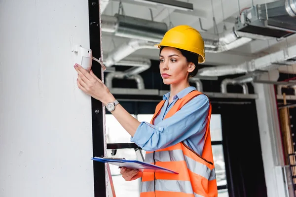 Beautiful firefighter checking fire alarm while holding clipboard — Stock Photo