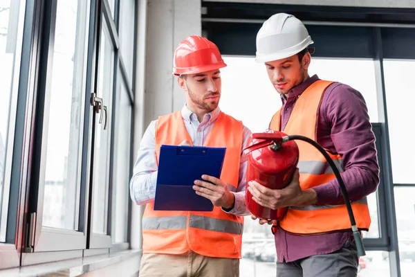 Firemen in helmets standing and looking at red extinguisher — Stock Photo