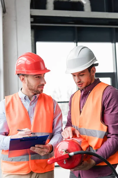 Fireman in helmet looking at coworker pointing with finger while holding red extinguisher — Stock Photo